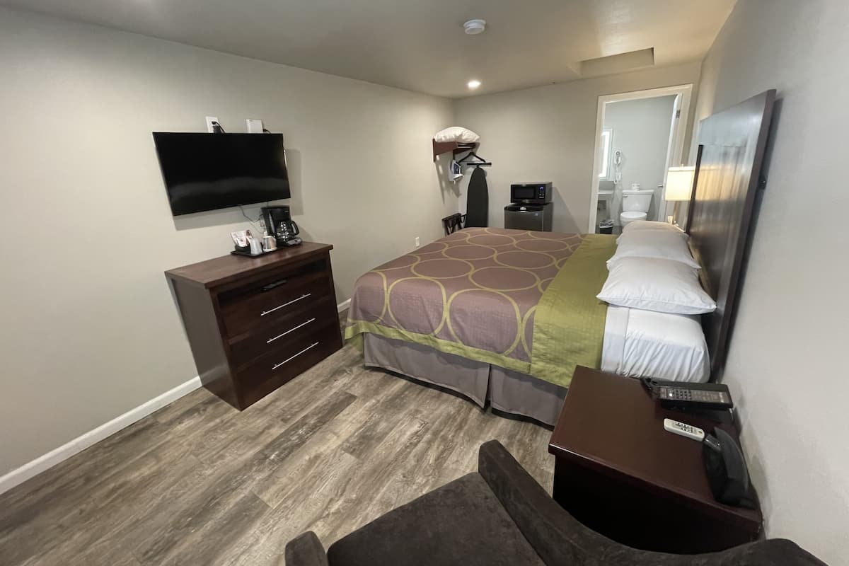 A hotel room with a bed, a TV mounted on the wall, a desk with a chair, a dresser, and a microwave.