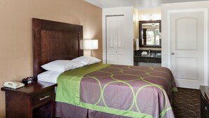 A hotel room with a bed, a nightstand with a phone and remote, a mirror, a door, and a bathroom visible through an open door. - Budget Lodge Eugene (Eugene)