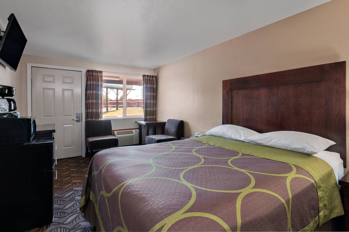 A hotel room with a bed, a desk, a chair, a television, and a window with curtains.