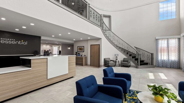 Eine moderne Hotelhalle mit einer Rezeption, einer blauen Sitzecke, einer Treppe und einem großen Fenster.