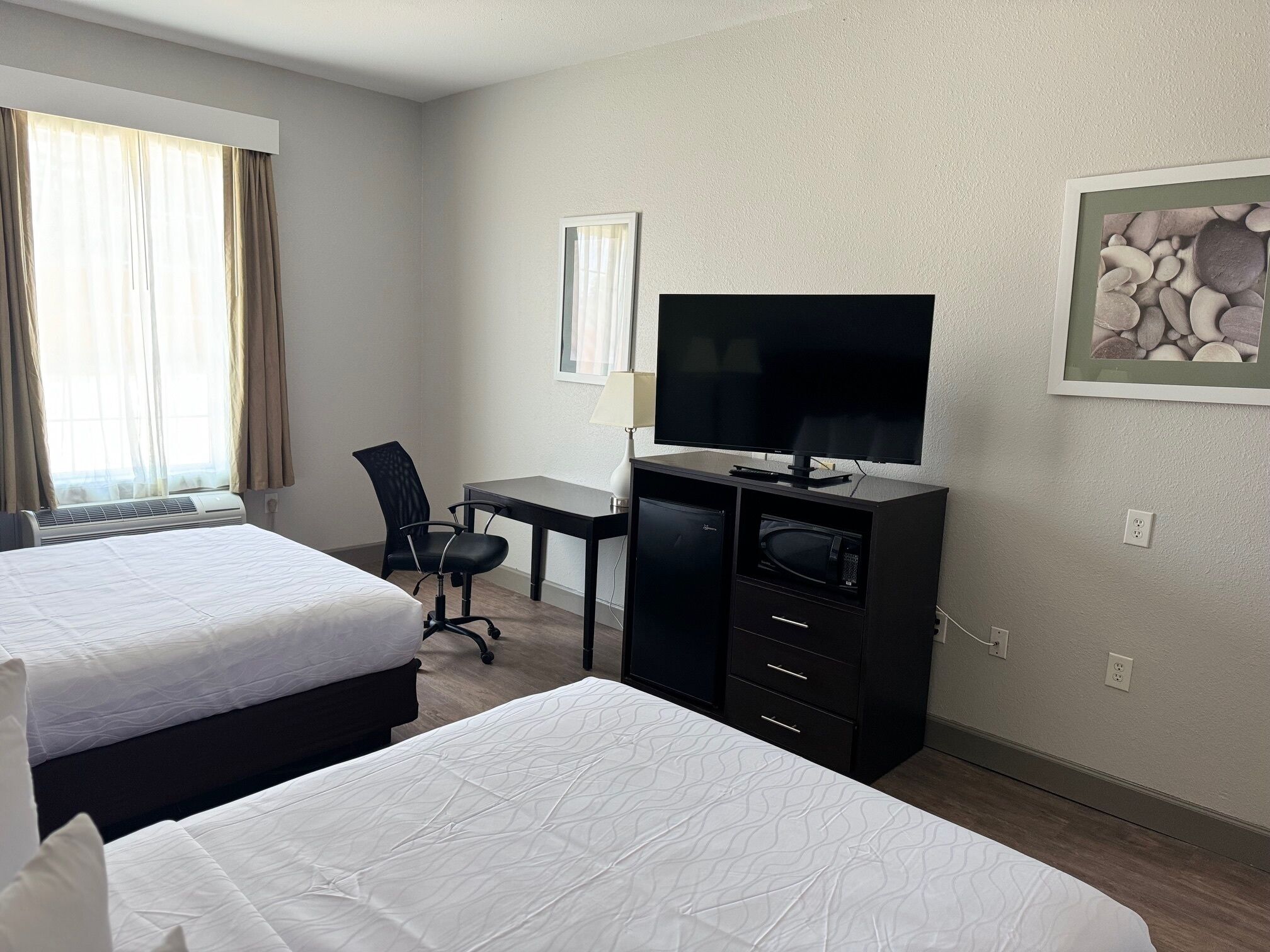 Habitación de hotel con dos camas, un escritorio con televisor, una silla y un cuadro en la pared.
