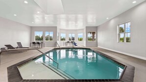 Ein Innenpool mit großen Fenstern, einer von der Sonne durchfluteten Decke und einem Poolbereich mit Stühlen und einem Tisch.