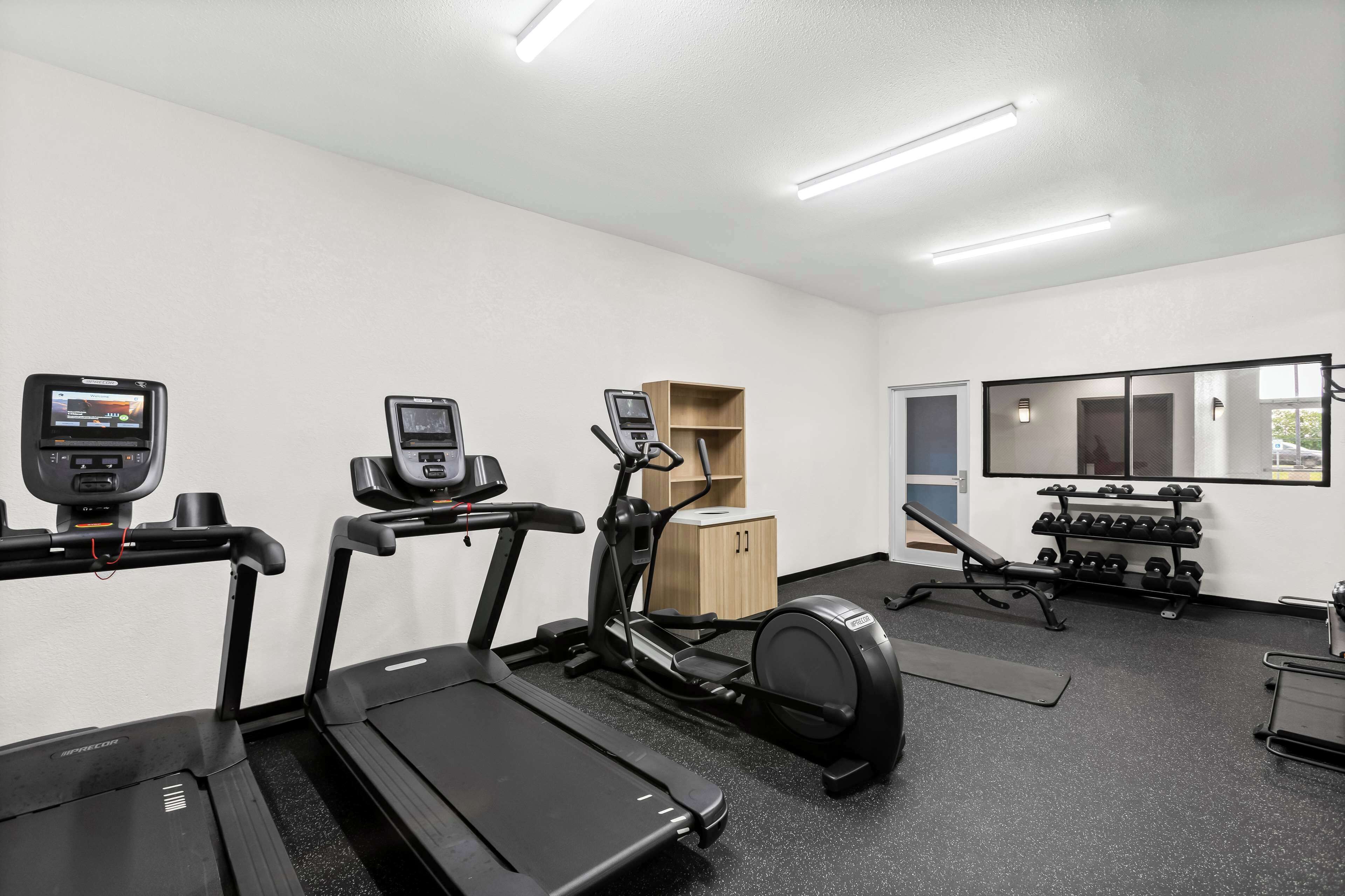 Ein Fitnessraum mit Laufbändern, Crosstrainern, einer Bank und einer Hantelbank.
