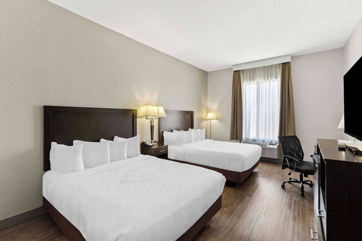 A hotel room with two beds, a desk, a chair, and a TV.