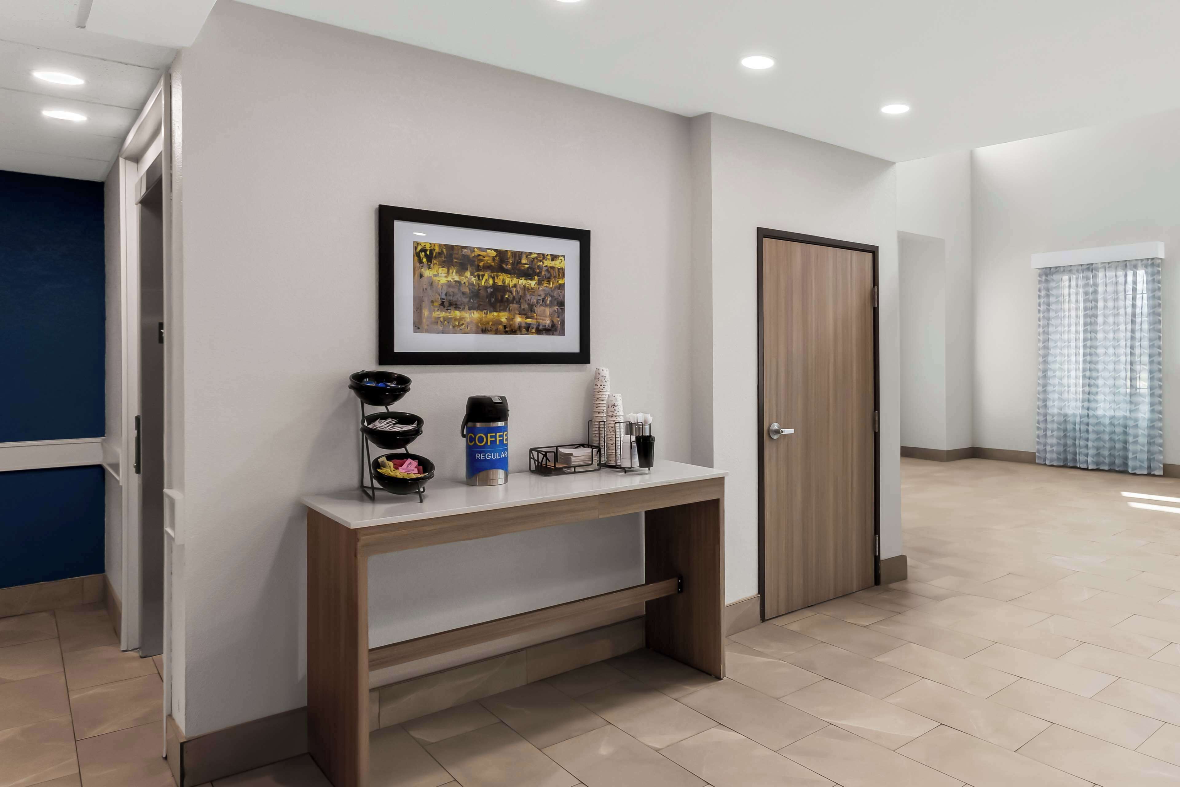Eine moderne Hotelhalle mit einem Holzkonsolentisch, einem gerahmten abstrakten Gemälde und einer Kaffeestation.