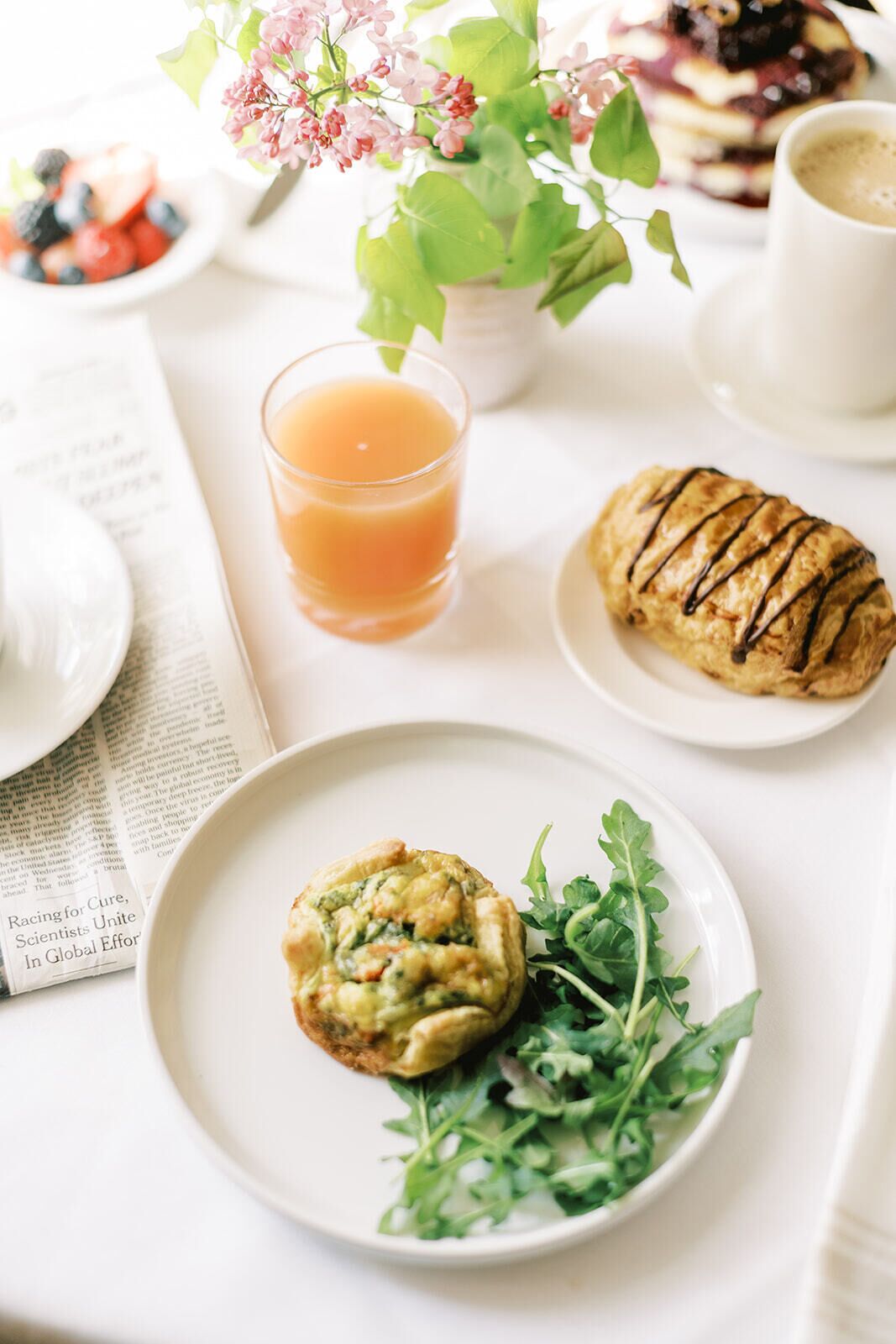 A breakfast setting with a plate of food, a glass of orange juice, a pastry, and a cup of coffee.