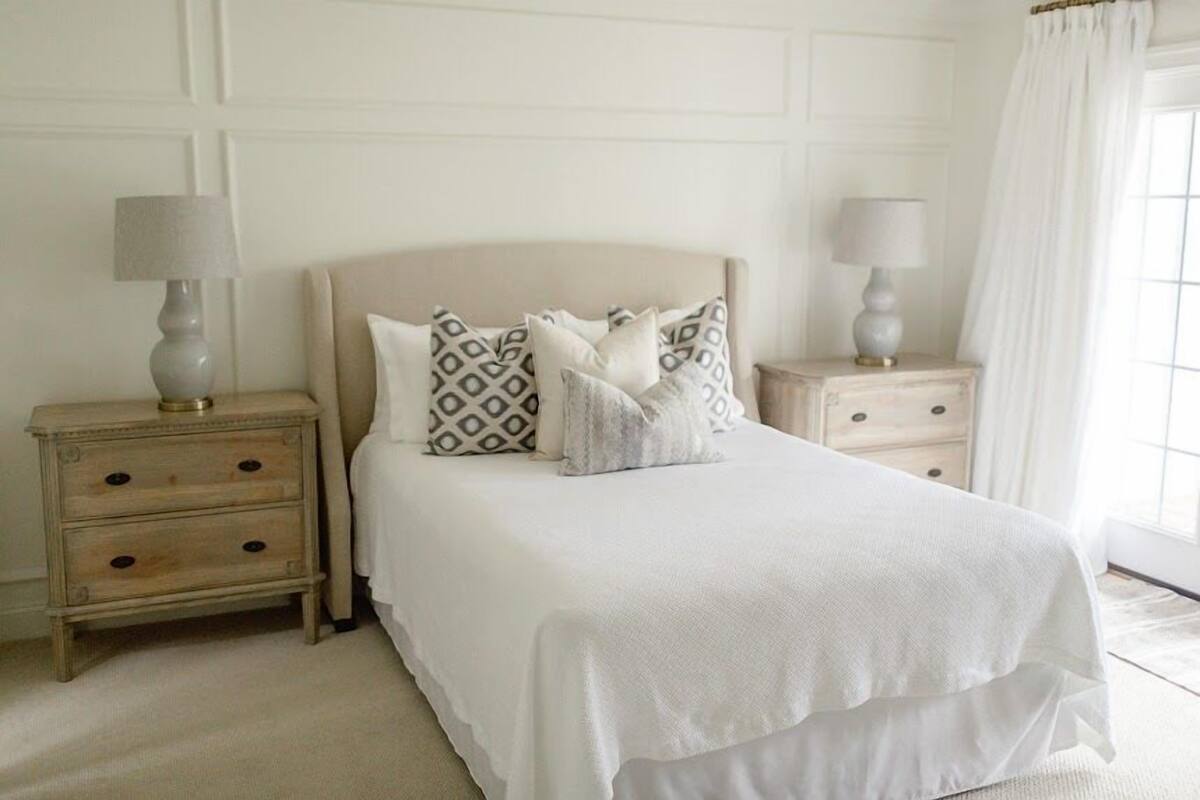 A neatly arranged bedroom with a large bed, two bedside tables with lamps, and a window with curtains.