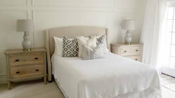 Une chambre bien rangée, avec un grand lit, deux tables de chevet dotées de lampes et une fenêtre avec des rideaux.