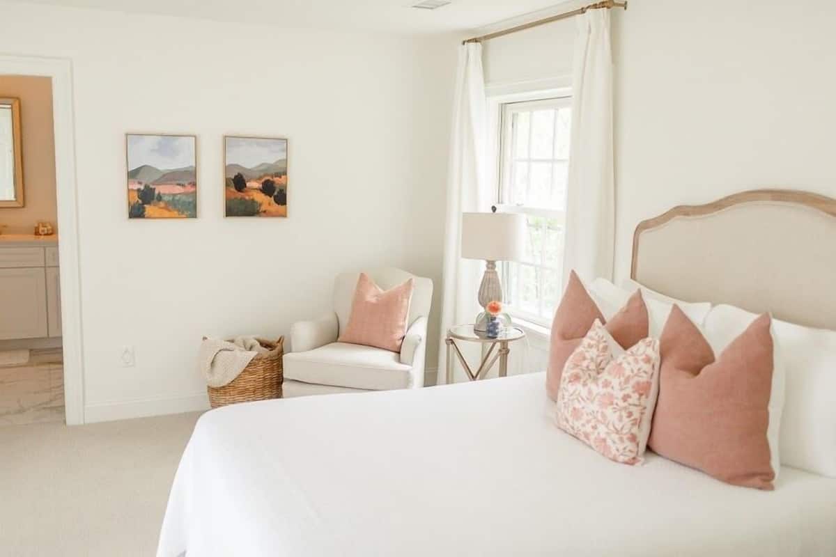 A bedroom with a bed, a chair, a lamp, and two paintings on the wall.