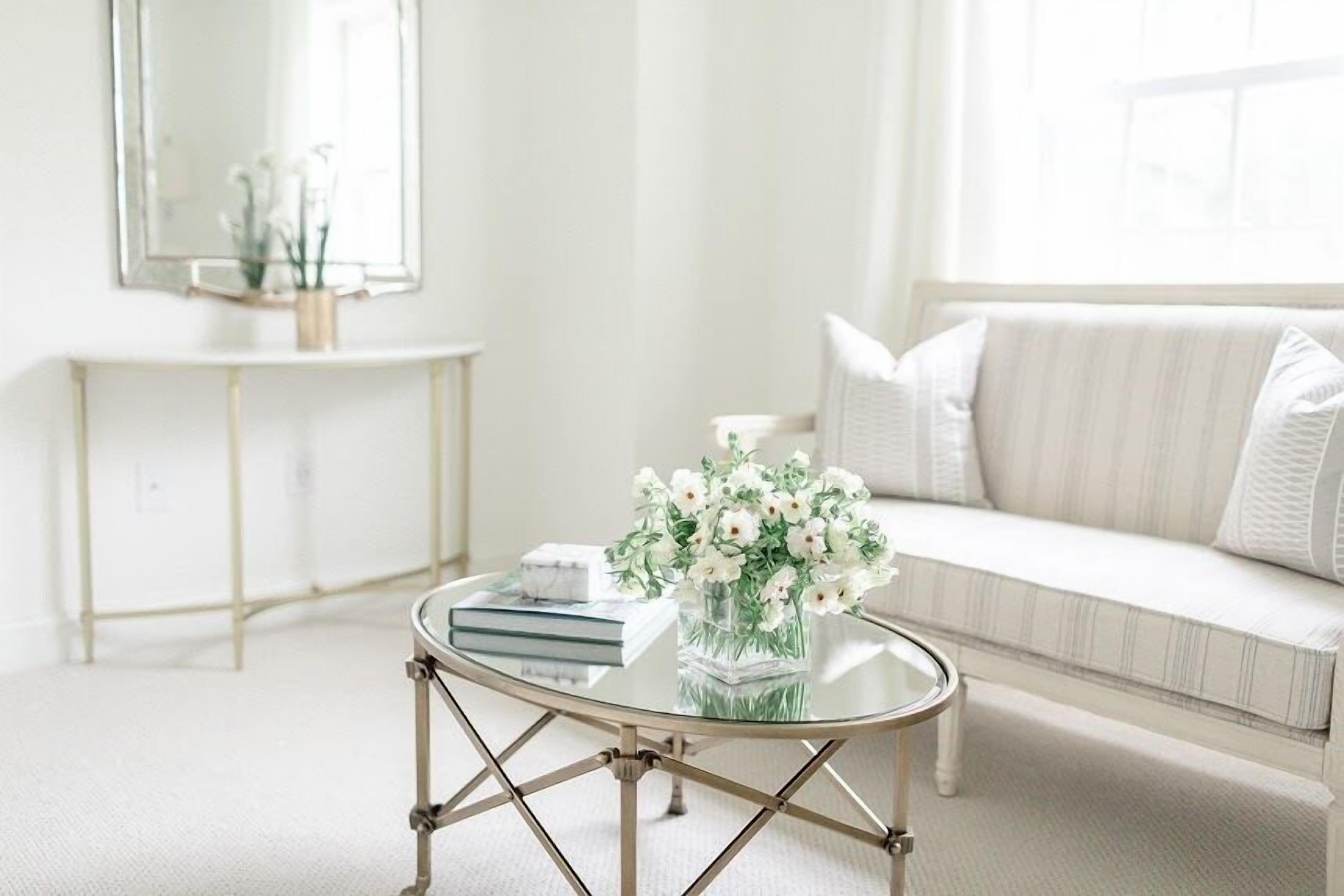 A modern living room with a glass coffee table, a white sofa, and a console table with a mirror and flowers.