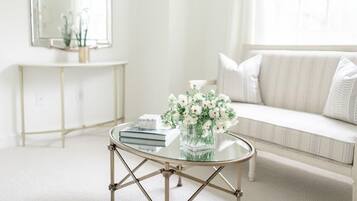 A modern living room with a glass coffee table, a white sofa, and a console table with a mirror and flowers.