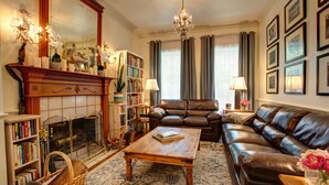 Una sala de estar con chimenea, sofá de cuero, estanterías y un candelabro.