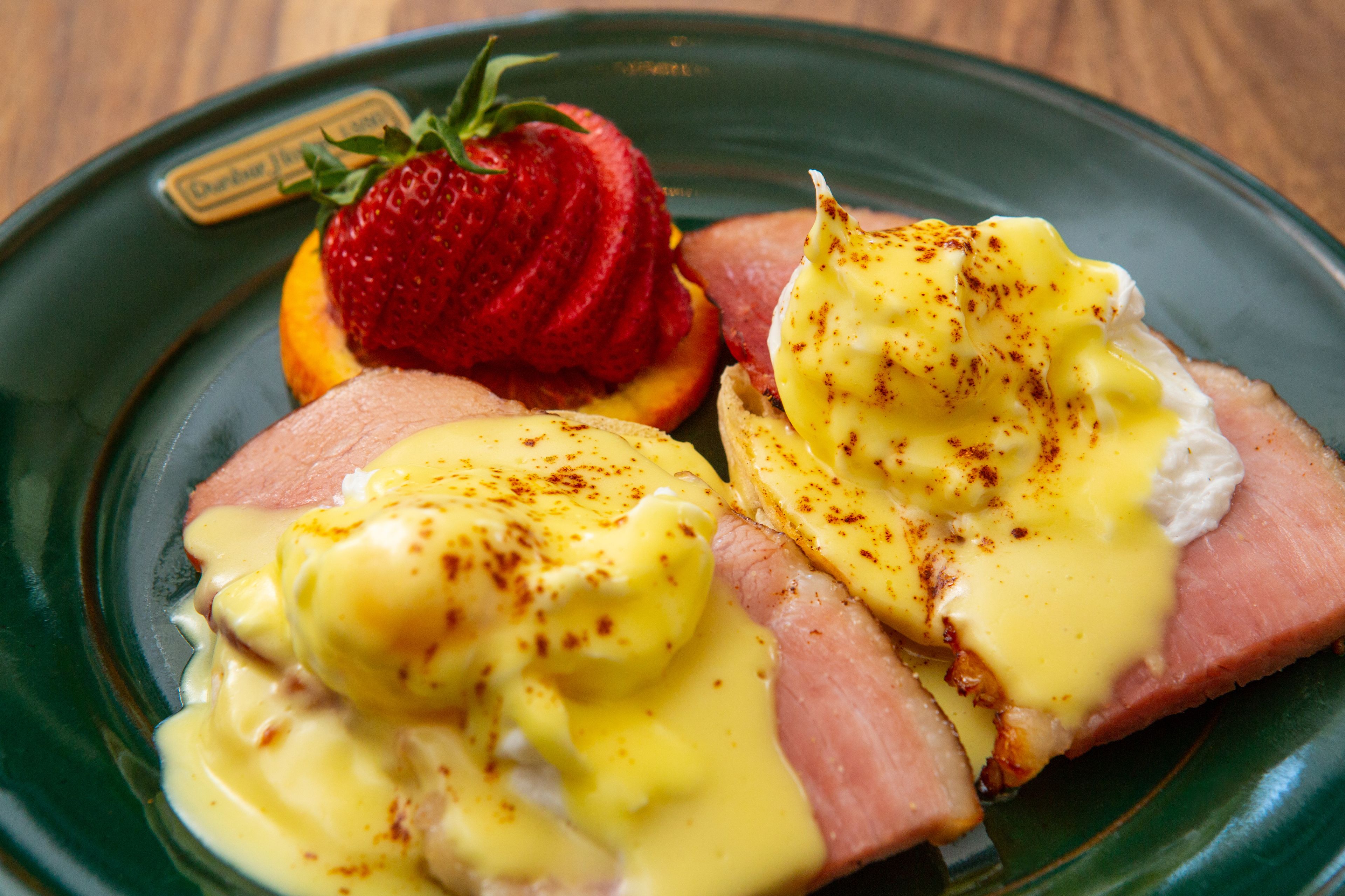 A plate with eggs benedict, ham, and a strawberry.