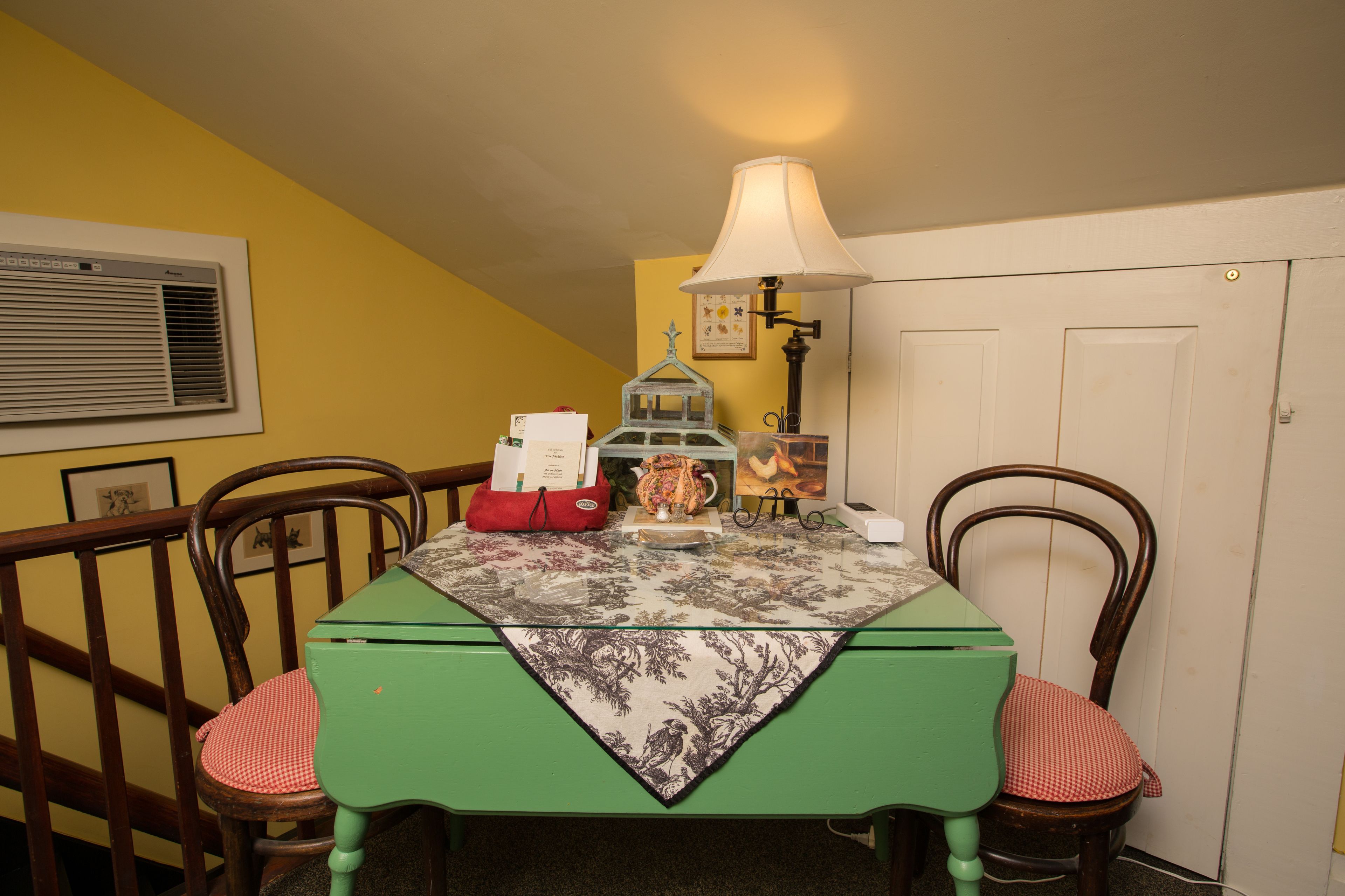 A dining table with a green tablecloth, two chairs, a lamp, and a decorative item on the table.