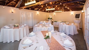 Un salón de banquetes con varias mesas redondas dispuestas para comer, que incluye manteles blancos, velas y centros de mesa con flores.