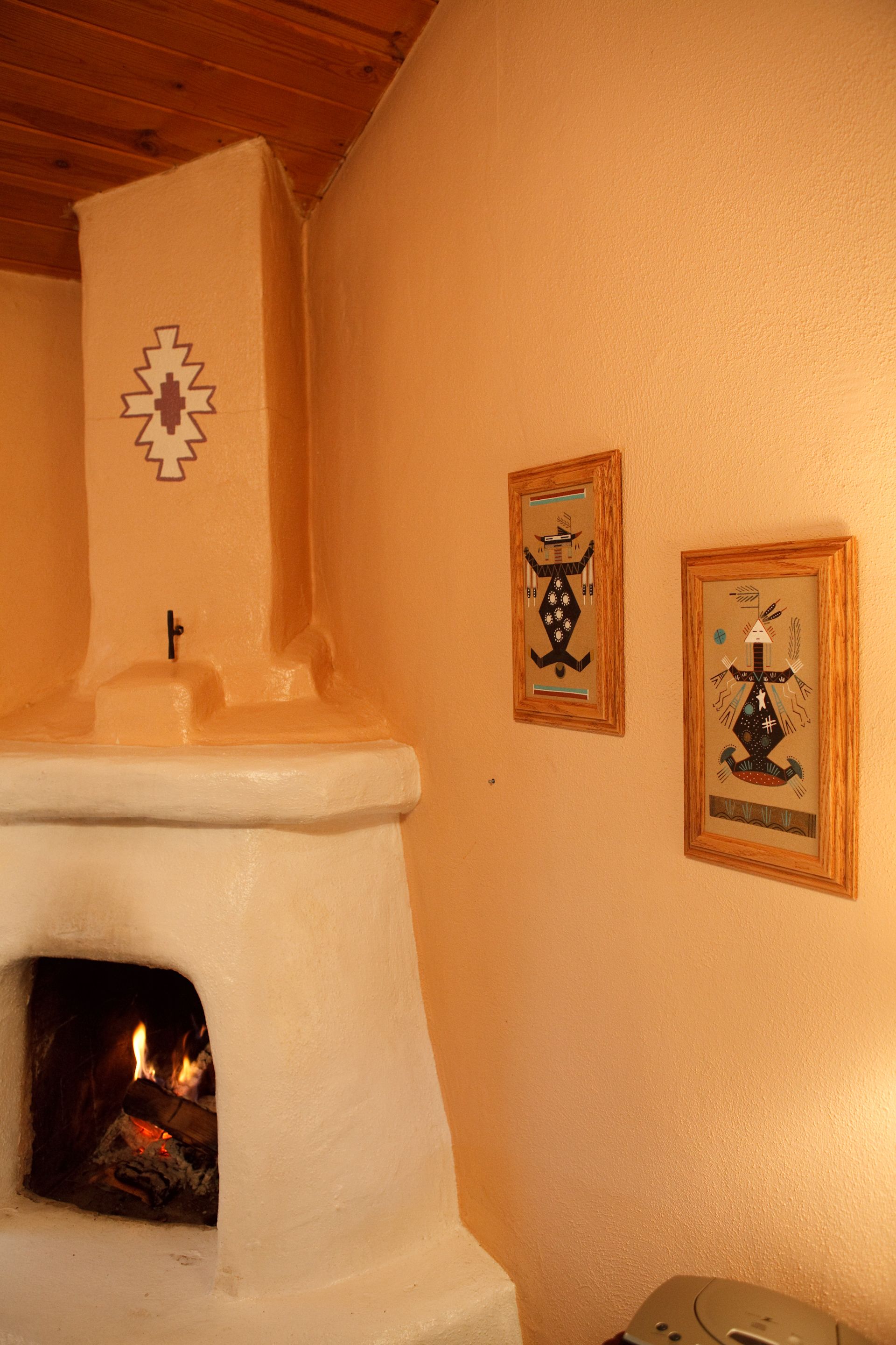 A fireplace with a fire, two framed artworks on the wall, and a wooden ceiling.