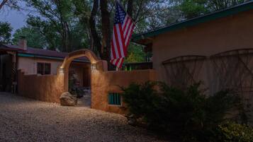 A rustic house with a distinctive arched entrance, an American flag, and a gravel driveway.