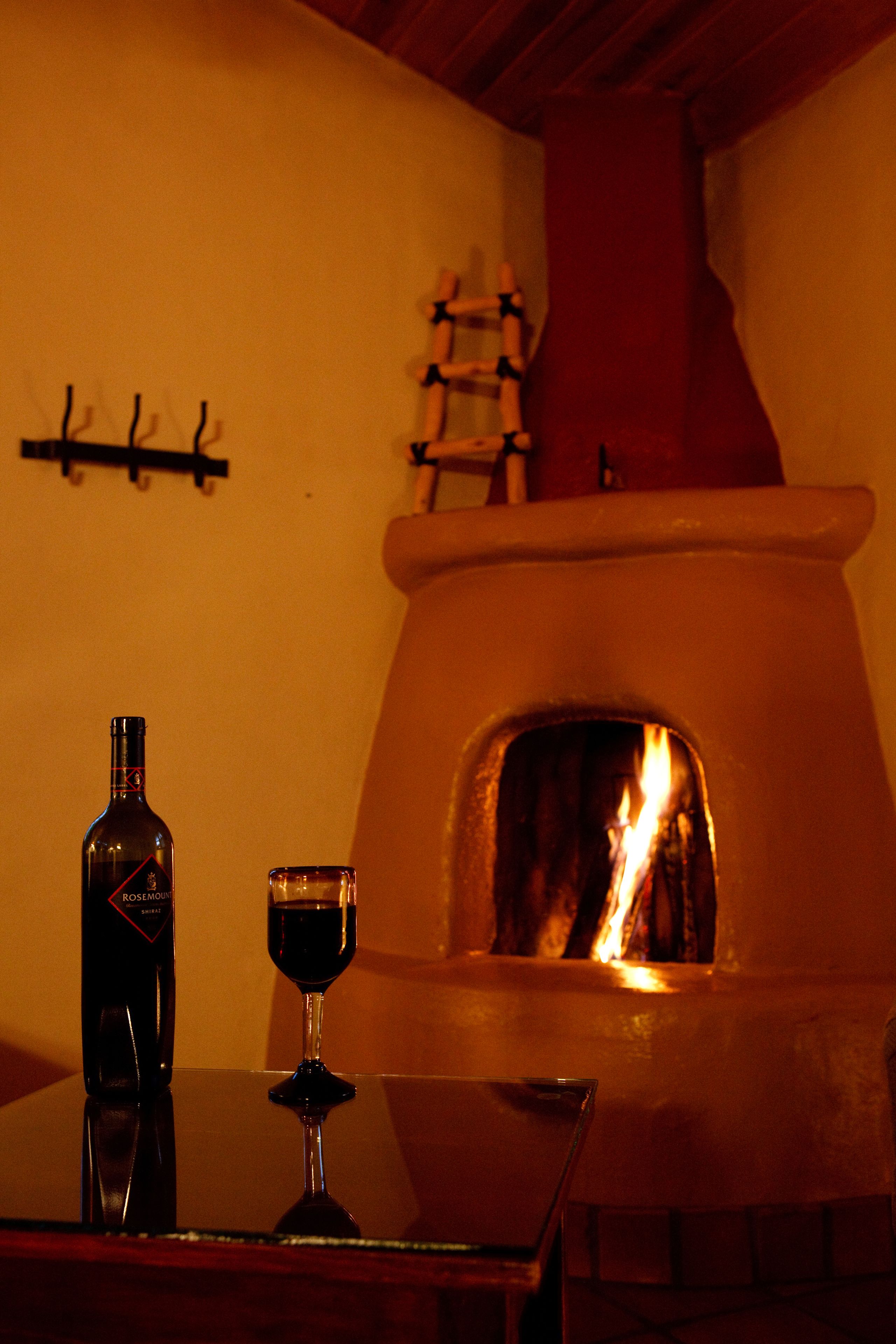 A table with a bottle and a glass, a fireplace, and a wall-mounted coat rack.