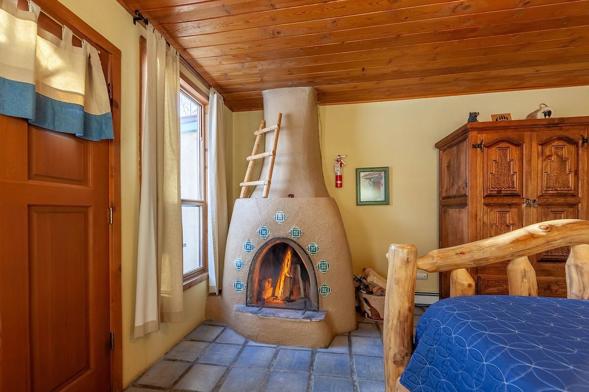 A room with a stone fireplace, wooden furniture, and a ladder leading to the fireplace.