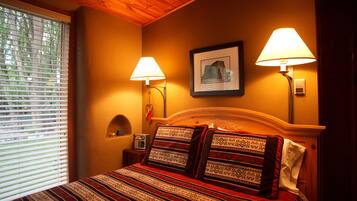 A bedroom with a wooden headboard, two bedside lamps, a framed picture on the wall, and a window with blinds.
