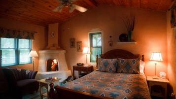 A cozy room with a fireplace, a bed with patterned bedding, a wooden ceiling, and a nightstand with a lamp.