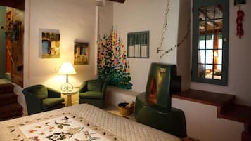 Une pièce chaleureuse avec un lit, deux fauteuils verts, une lampe, un mur orné d’une fresque colorée et un plafond en bois.