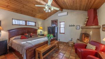 A cozy room with a wooden ceiling, a bed with a headboard, a wooden bench, a red leather chair, a fireplace, and a television.
