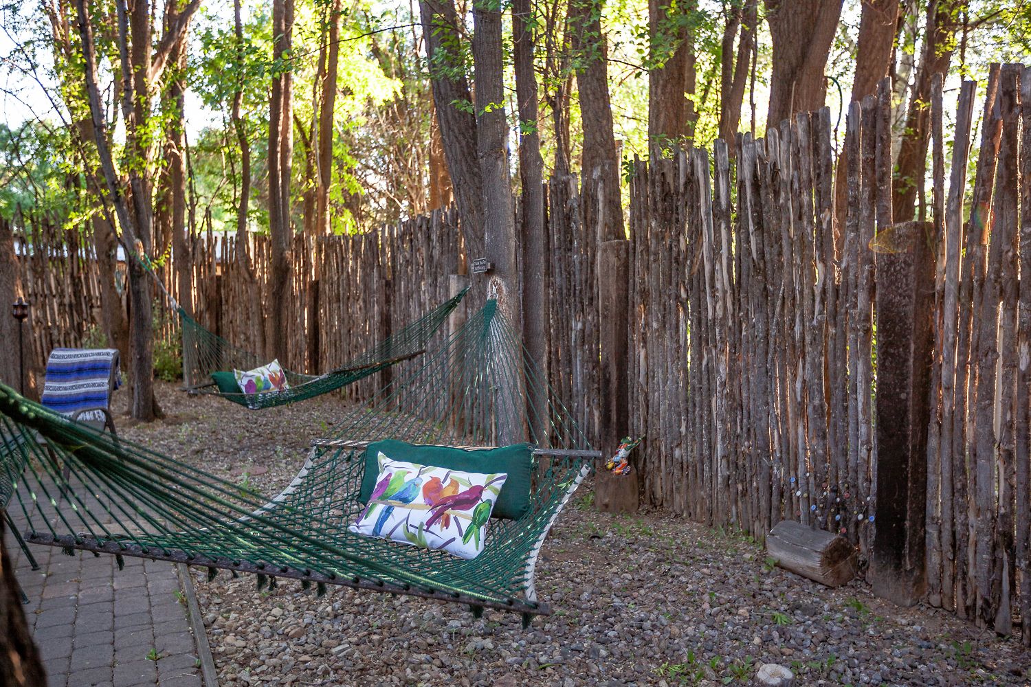 Una hamaca instalada en un área boscosa, con una valla de madera al fondo.