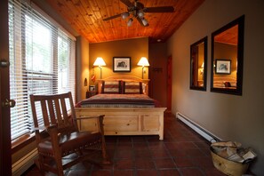 A bedroom with a wooden bed, two bedside lamps, a wooden chair, a ceiling fan, and a fireplace. - Dreamcatcher Bed and Breakfast (Taos)