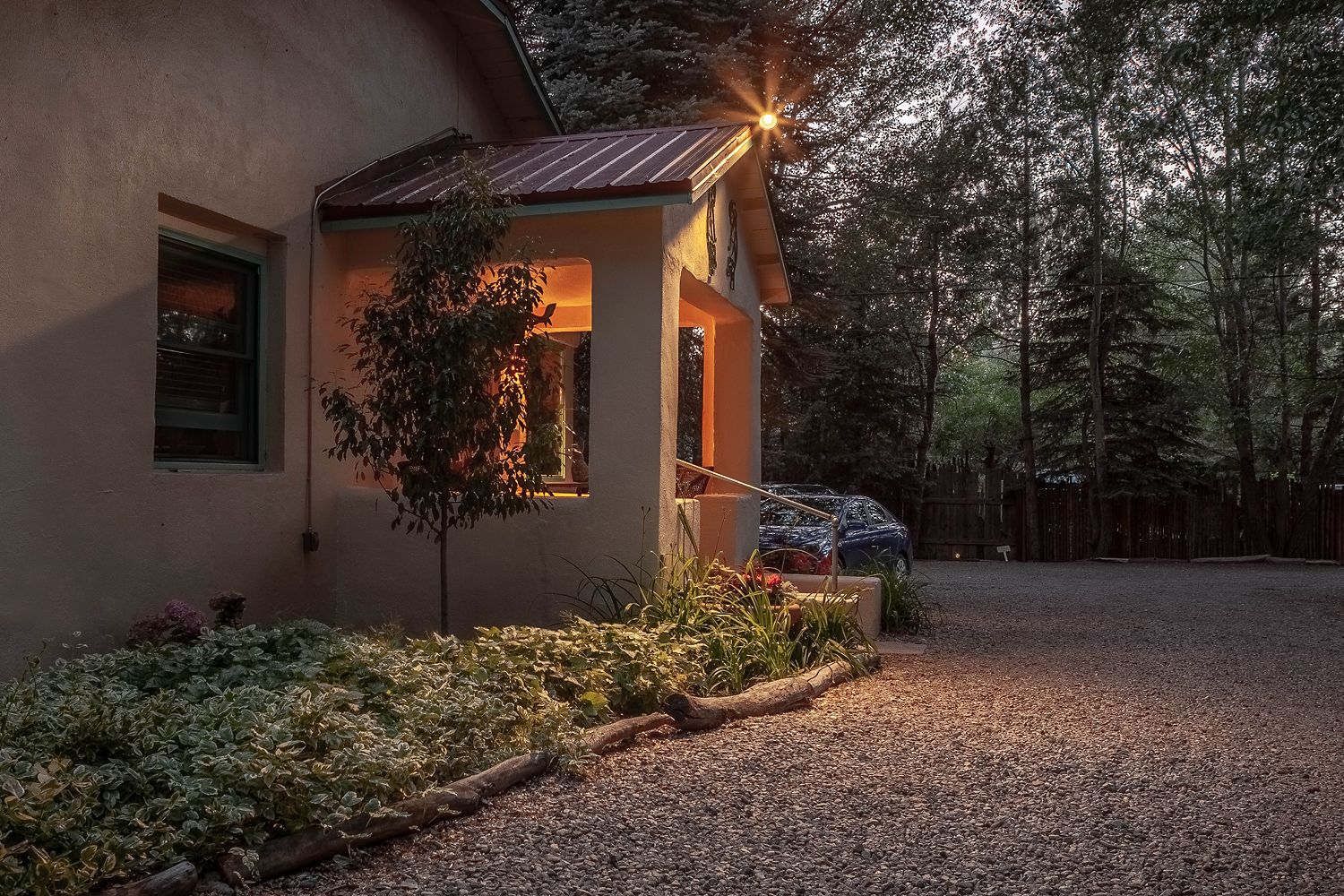 A house with a small porch, a tree, and a gravel driveway.