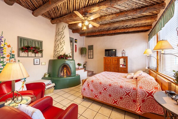 Um quarto acolhedor com lareira, cama com roupa de cama estampada, sofá vermelho e televisão.