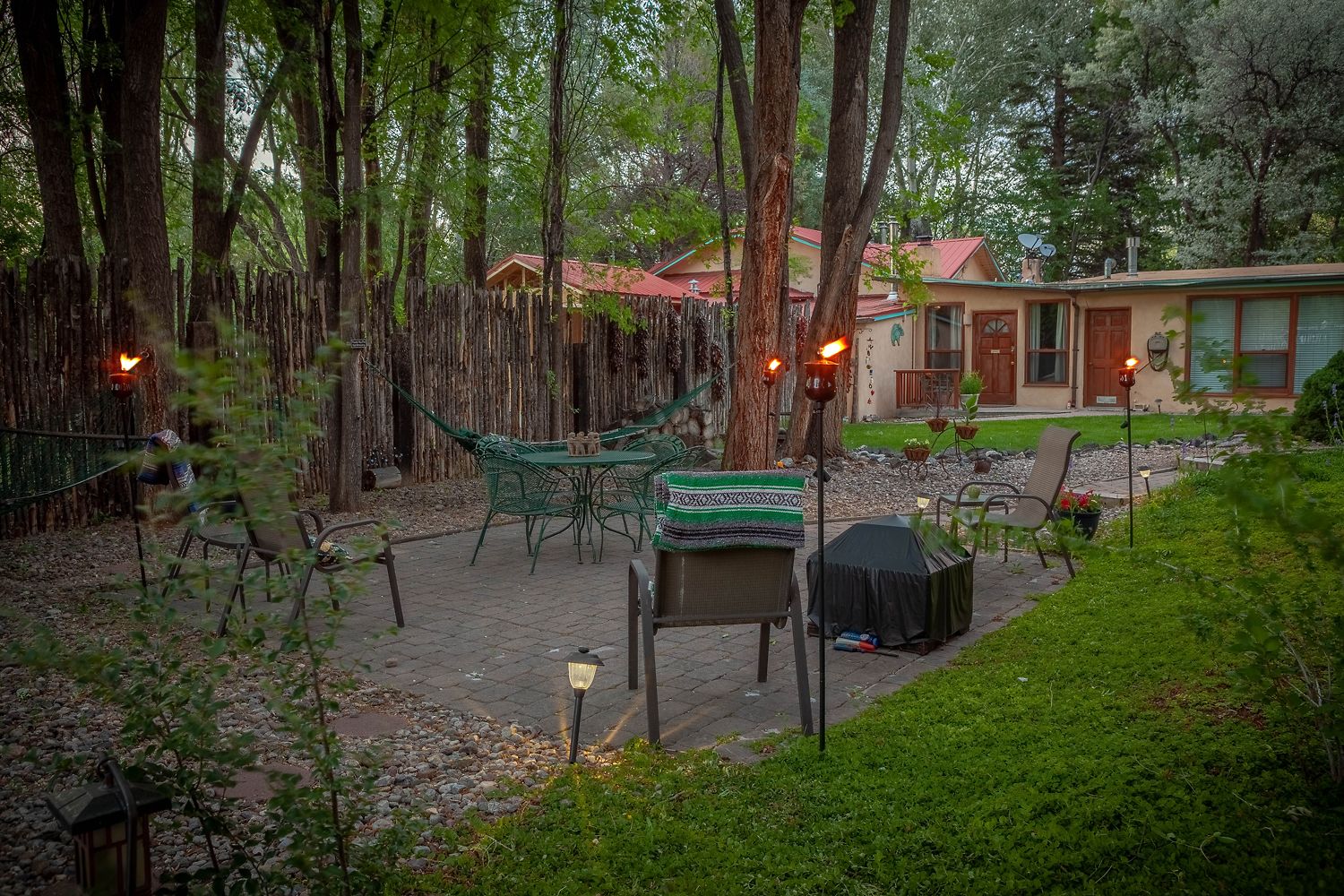 A rustic outdoor seating area with a hammock, a covered grill, and a patio table.