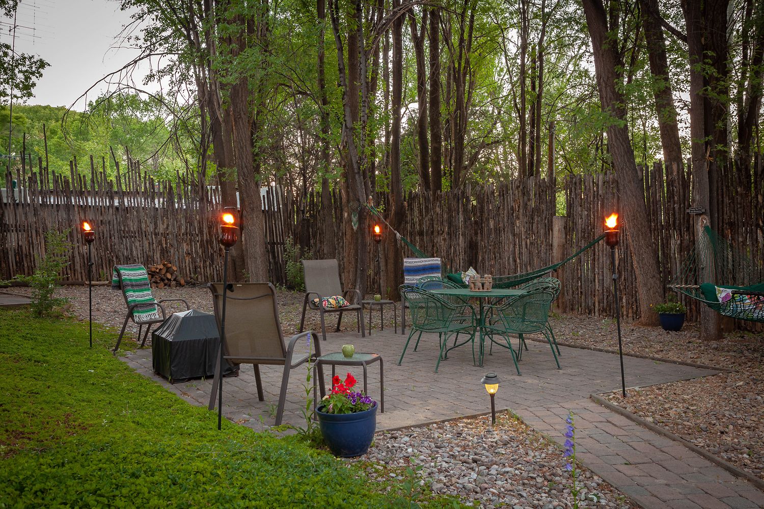 Un espace extérieur aménagé en patio, avec des sièges, un hamac et des torches décoratives.
