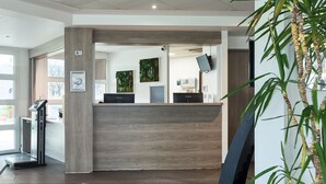 A reception area with a wooden reception desk, a scale, and a potted plant. - Zenitude Hôtel - Résidences Roissy Village (Roissy-en-France)