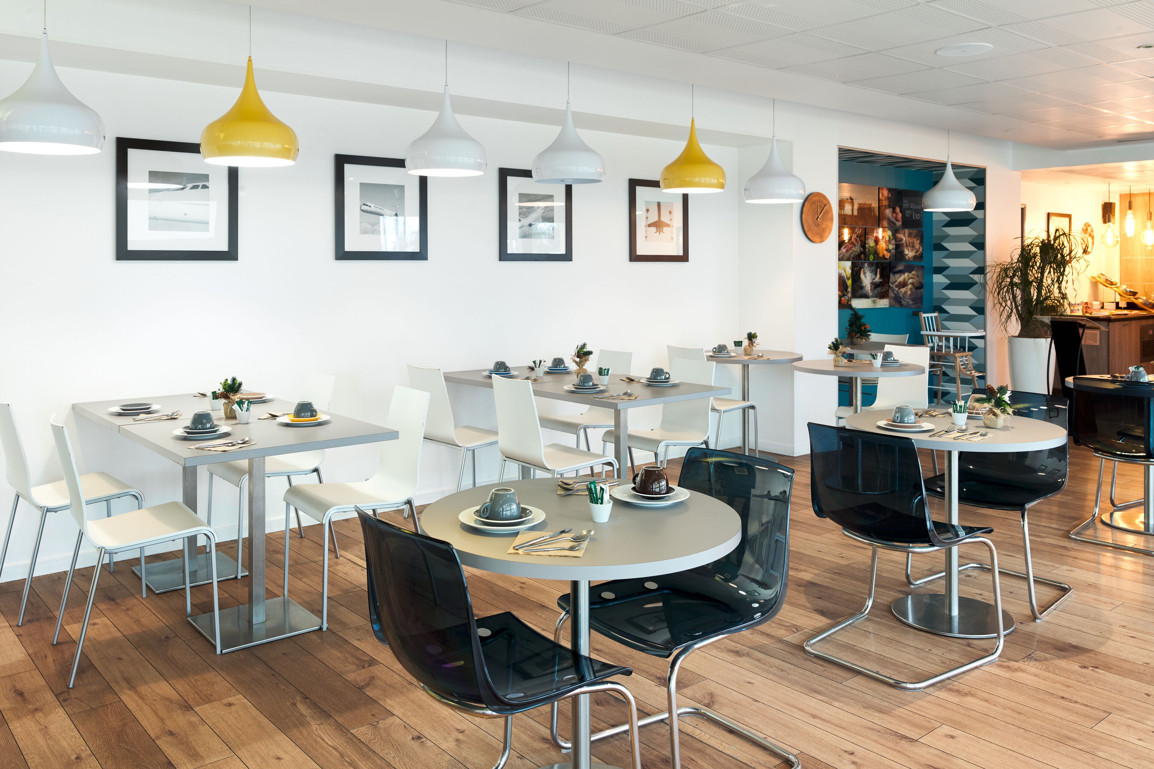 A modern dining area with multiple tables and chairs, featuring pendant lighting and framed artwork on the walls.