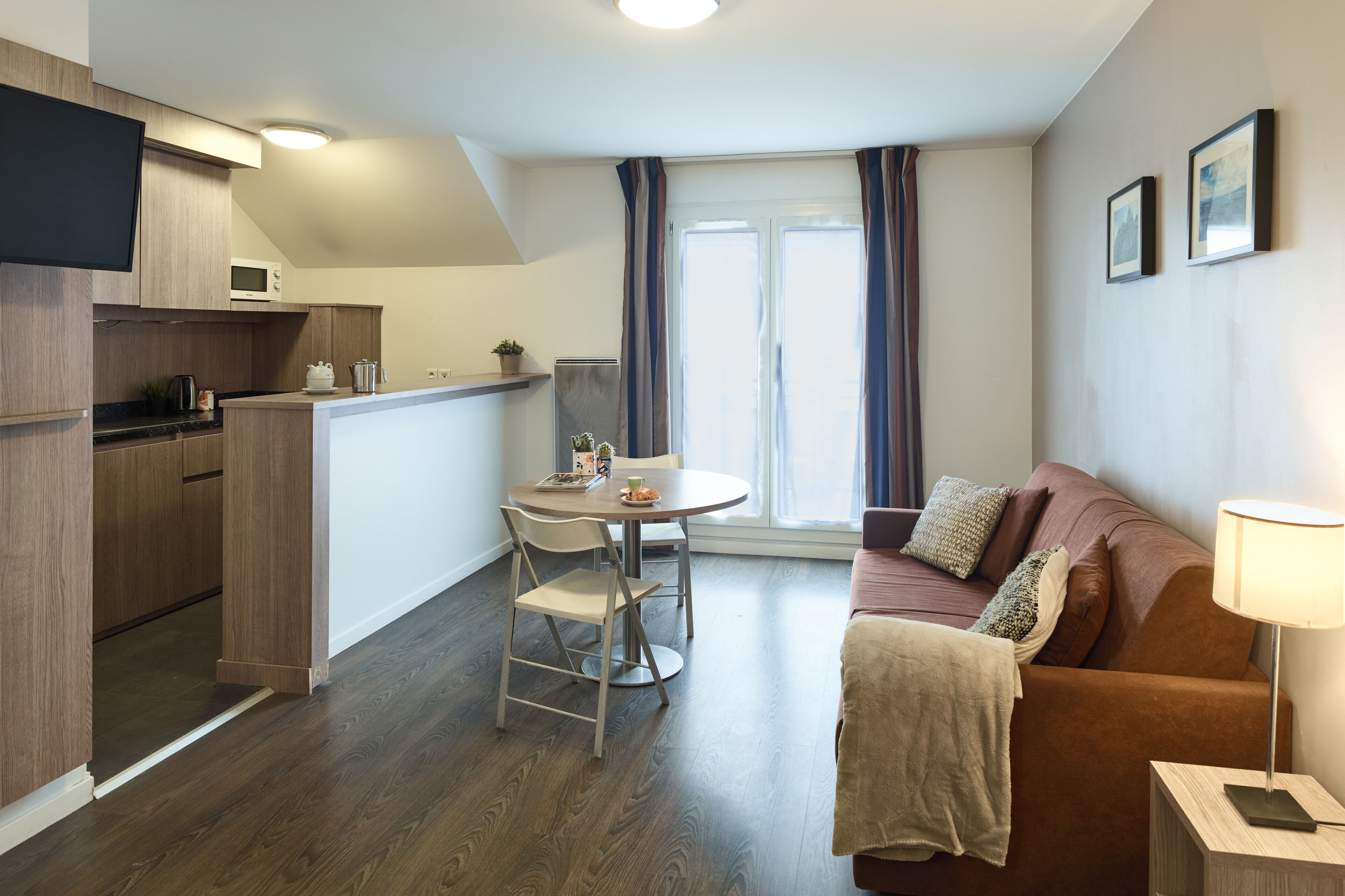 Ein kompakter Wohnbereich mit Küchenzeile, Essbereich und einer Sitzecke mit Sofa und Lampe.