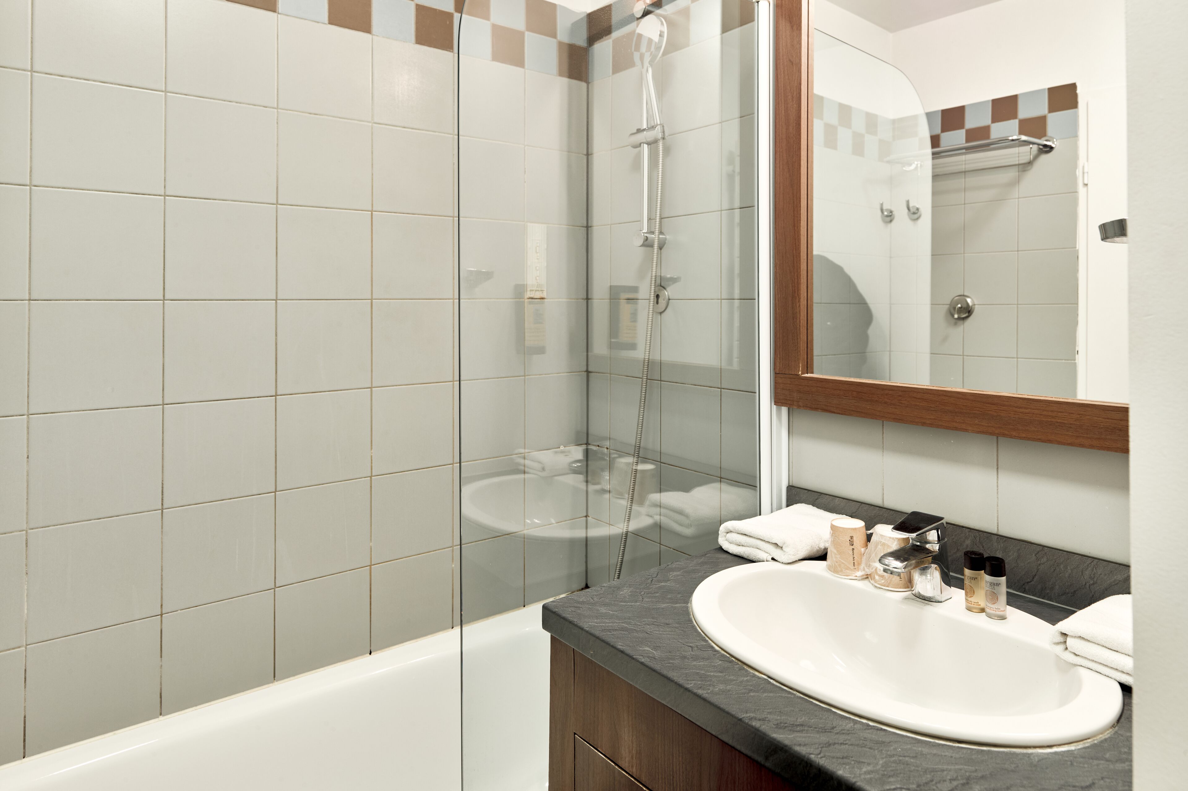 Un bany modern amb dutxa tancada amb vidre, una banyera blanca i un lavabo amb sabó i altres productes de tocador.