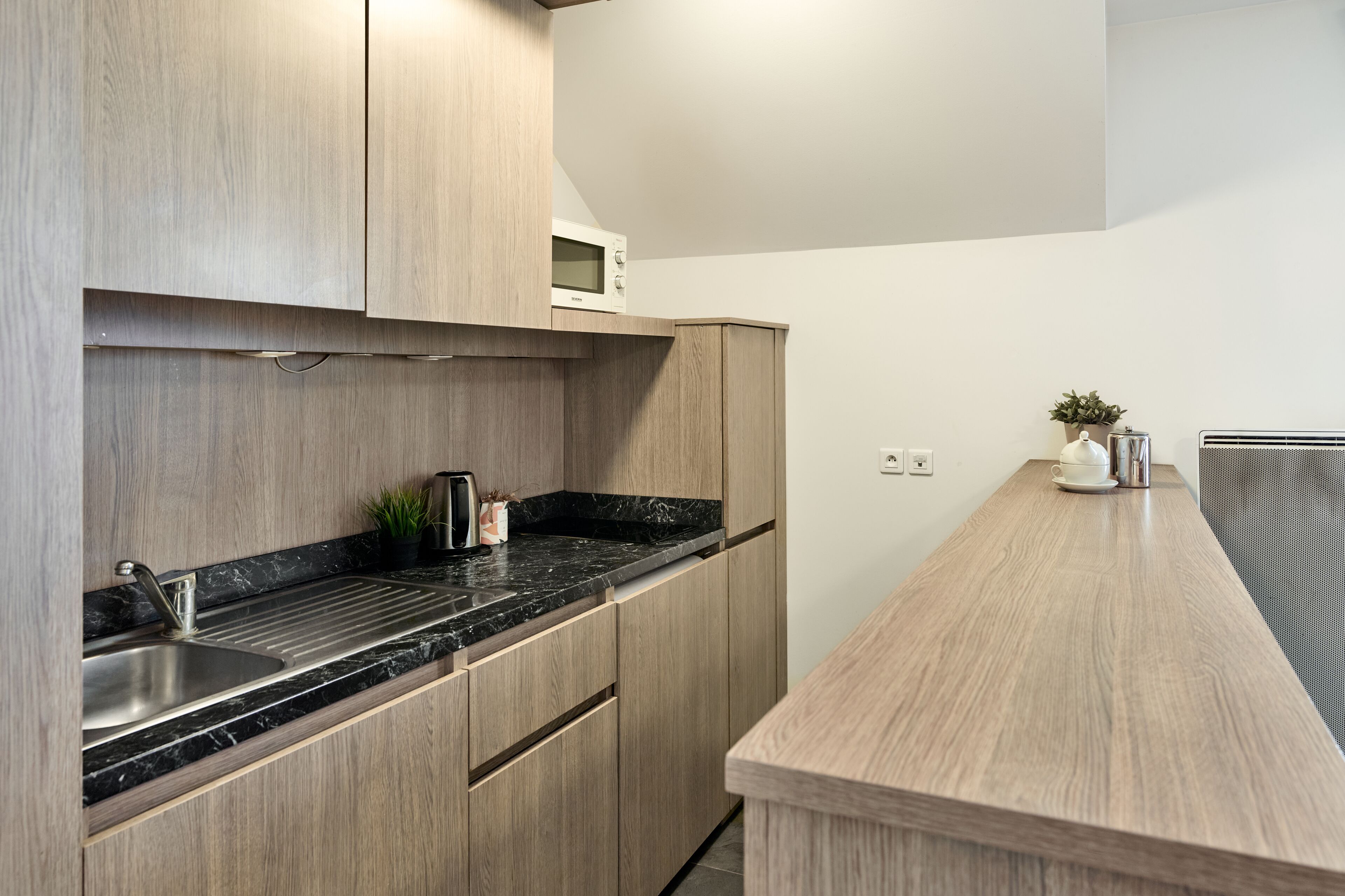 Une cuisine moderne avec des meubles en bois, un plan de travail noir et un four à micro-ondes.