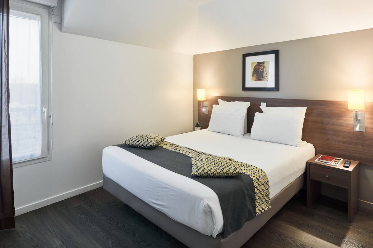 A neatly made bed with white and patterned bedding, a bedside table with a lamp, and a framed picture on the wall.