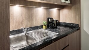 A modern kitchen with a stainless steel sink, a black marble countertop, wooden cabinets, and a built-in microwave. - Zenitude Hôtel - Résidences Roissy Village (Roissy-en-France)