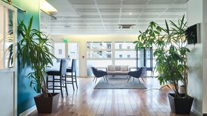 A modern interior with wooden flooring, two potted plants, a sofa, and a dining area with chairs. - Zenitude Hôtel - Résidences Roissy Village (Roissy-en-France)