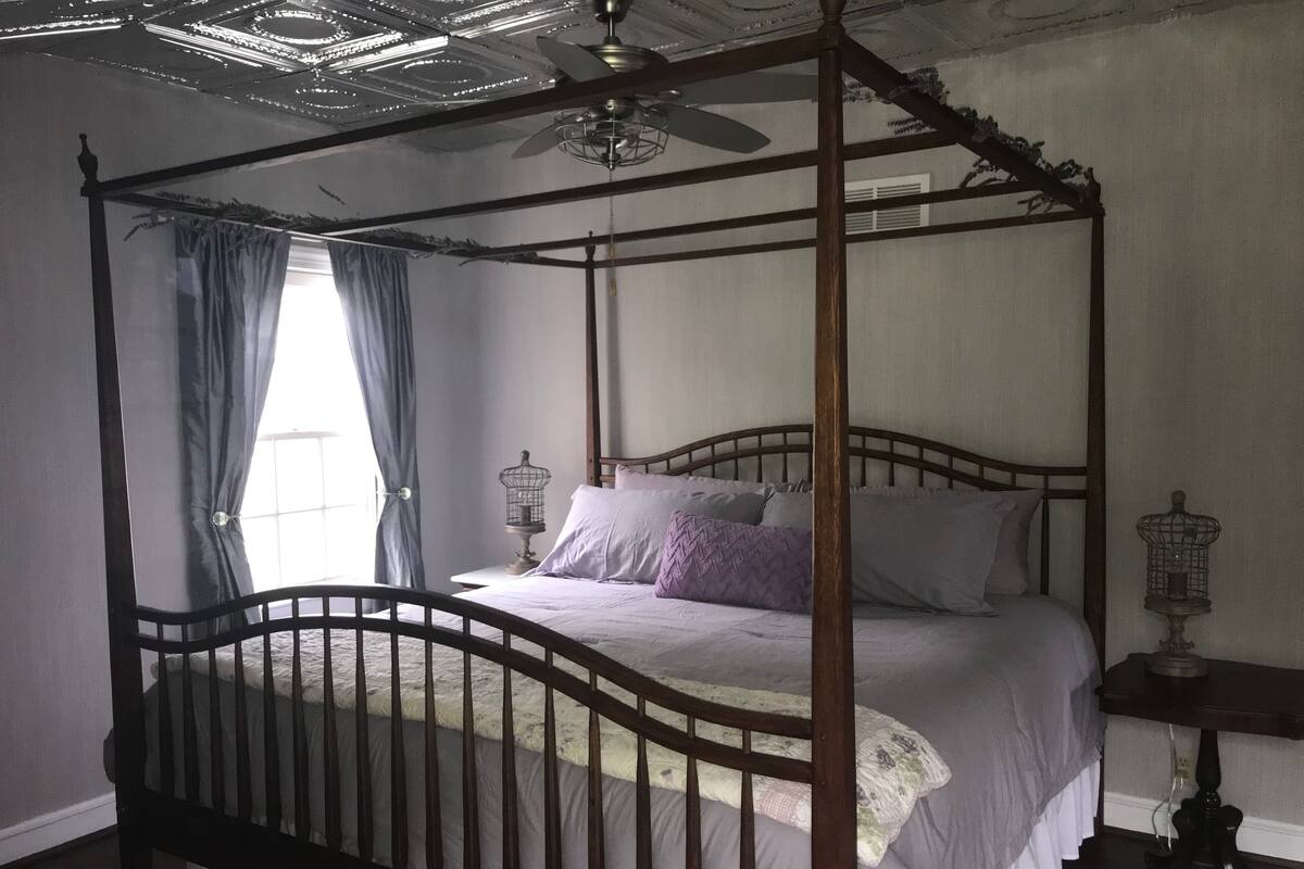 Un lit à baldaquin à quatre poteaux, avec une structure en bois, un ventilateur de plafond et deux tables de chevet surmontées de cages à oiseaux.