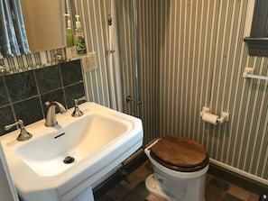 A bathroom with a white sink, two faucets, a wooden toilet seat, and striped wallpaper. - Wild Wisteria (Chadds Ford)