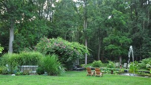 A lush garden with a pond, wooden chairs, and a white fence. - Wild Wisteria (Chadds Ford)