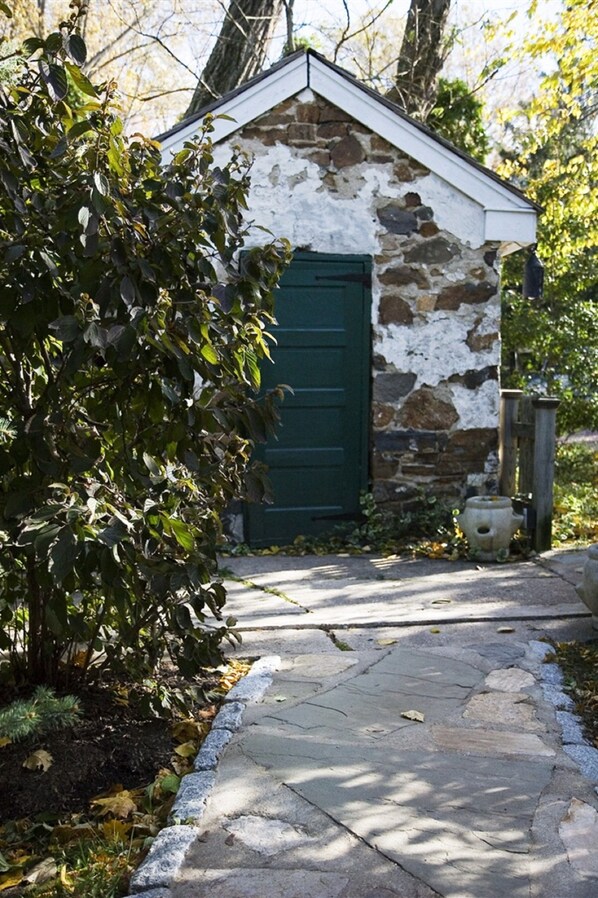 A stone building with a green door, a stone pathway leading to it, and a bush in the foreground.
