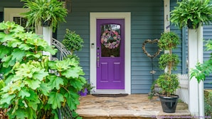 A purple front door with a wreath, surrounded by potted plants and a heart-shaped decoration. - Wild Wisteria (Chadds Ford)