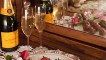 A bedroom with a wooden bed, a bedside table with champagne bottles and glasses, and a tray with strawberries and flowers.