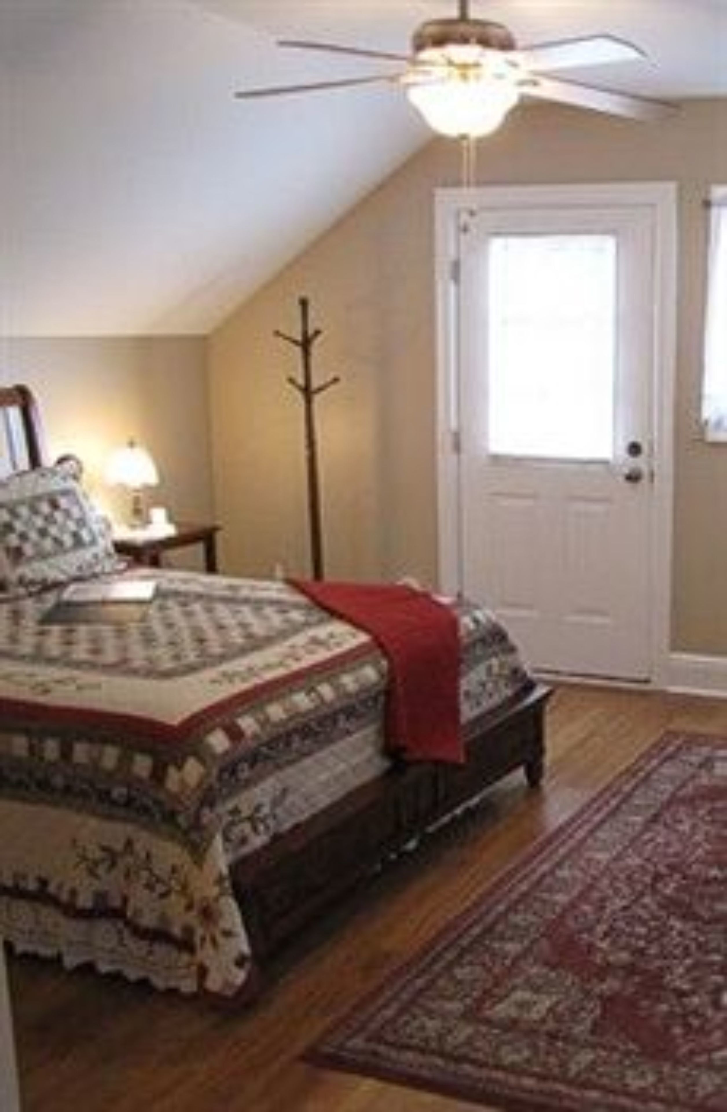 Quarto com cama, ventoinha no teto, porta e janela.