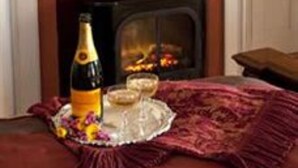 A fireplace with a mantel, a vase with yellow flowers, and a bottle of champagne on a table.