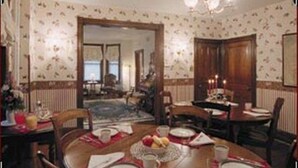 A dining room with a round table set for four, a chandelier, and patterned wallpaper.
